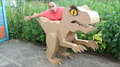 a man is sitting on top of a cardboard dinosaur in front of some bushes and plants