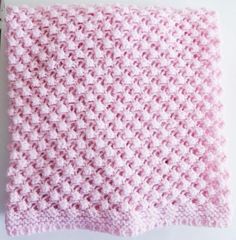 a pink crocheted blanket sitting on top of a white table next to a pair of scissors