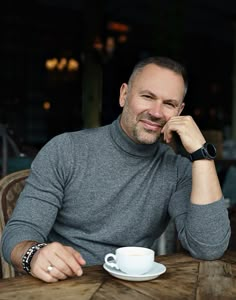 a man sitting at a table with a coffee cup and saucer in front of him