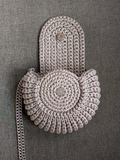 a crocheted purse sitting on top of a gray surface next to a chain