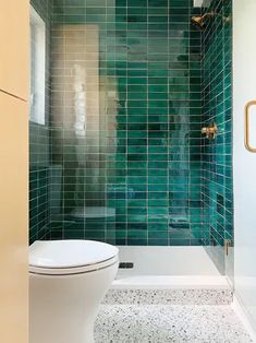 a white toilet sitting next to a walk in shower under a green tiled bathroom wall