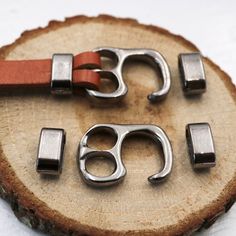 two metal objects sitting on top of a piece of wood next to a leather strap