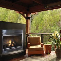 a living room with a fire place and chairs on the deck overlooking trees in the distance