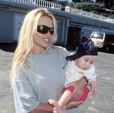 a woman is holding a baby in her arms and smiling at the camera while wearing sunglasses