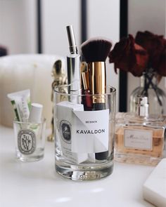 a close up of a cup on a table with makeup brushes and other items in it