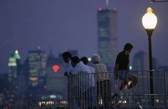 some people are standing on a bridge looking at the city lights and skyscrapers in the distance