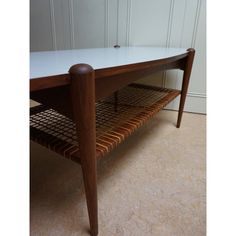 a wooden table with a white top and two shelves on the bottom, in front of a wall