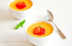 two white bowls filled with soup and topped with a strawberry