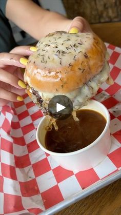 a person is dipping something into a bowl with sauce on the table next to a bagel