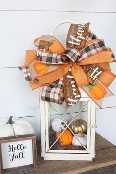 a white lantern filled with pumpkins on top of a wooden table next to a sign that says happy fall