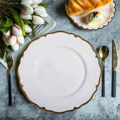 an empty white plate with gold trim sits on a table next to silverware and flowers