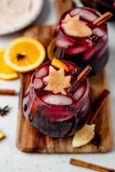 two glasses filled with liquid and garnished with orange slices on a cutting board