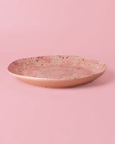 a pink plate with speckles on it against a light pink background in the shape of a bowl