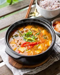 there is a bowl of soup with tofu and vegetables on the table next to rice