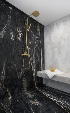 a bathroom with black marble walls and flooring, shower head and hand held faucet