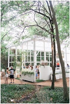 a group of people standing in front of a white building surrounded by trees and bushes