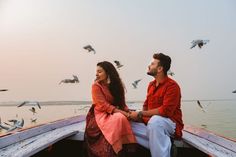 a man and woman sitting on the back of a boat with seagulls flying above them