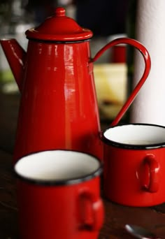 two red teapots and one white cup are sitting on a table next to each other