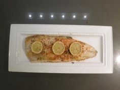 a fish with lemon slices on it is displayed in a white plate and silver surface