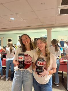 two girls are holding up their coke cans in front of the camera while standing next to each other