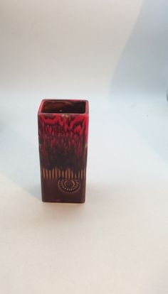 a red and black vase sitting on top of a white table next to a cup