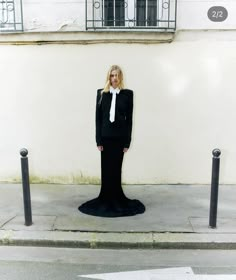 a woman wearing a black suit and white tie standing in front of a tall building