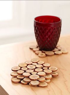 a red glass cup sitting on top of a wooden table next to some cut up wood slices