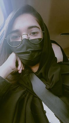 a woman with glasses and a black mask covering her face while sitting in a car