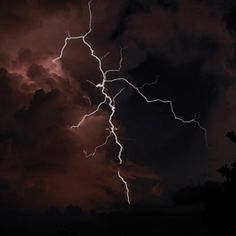 a lightning bolt is seen in the sky above some trees and dark clouds at night