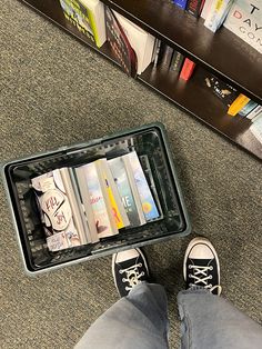 a person standing in front of a book shelf with their feet on an open suitcase