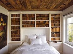 a white bed sitting in a bedroom next to a bookshelf filled with lots of books