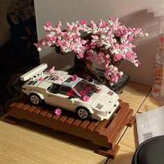 a toy car is parked under a tree with pink flowers on the roof and in the trunk