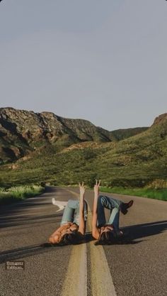 two people laying on the road with their arms in the air and one person holding his head up