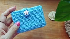 a hand holding a small blue crocheted wallet with a flower on it and a coin