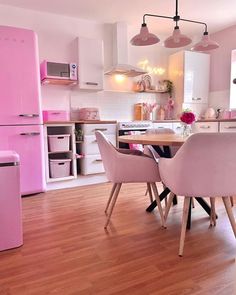 a pink refrigerator and table in a room with wooden floors, white walls and cabinets