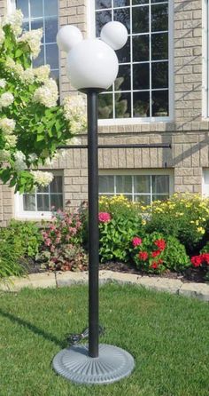 a lamp that is on top of a pole in front of some flowers and bushes