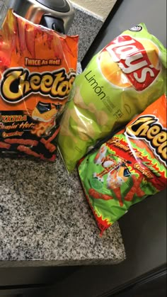 two bags of cheetos and a can of soda sitting on a granite counter top