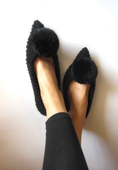 a person's feet wearing black slippers with fuzzy fur on them, against a white wall