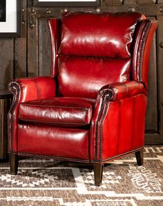 a red leather recliner chair sitting in front of a wooden paneled wall with framed pictures on it