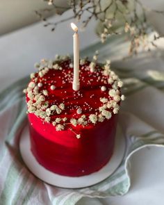 a red cake topped with a single candle and sprinkles on top of it