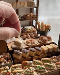 a person is picking up some bread from a table full of sandwiches and pastries