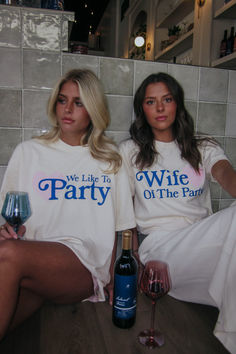 two women sitting next to each other wearing matching shirts and holding wine glasses in their hands