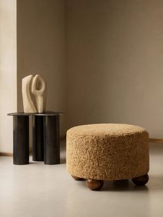 a round ottoman sitting next to a table with a sculpture on it's side