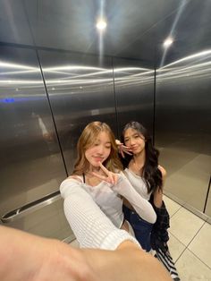 two girls standing in front of an elevator pointing at the camera with their fingers together