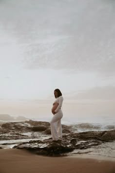 a pregnant woman standing on top of a beach next to the ocean