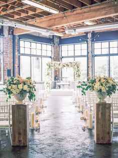 an indoor wedding venue with white chairs and floral centerpieces on wooden pillars, candles and flowers in vases