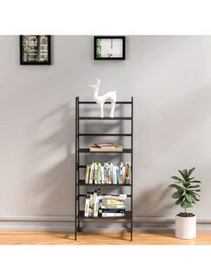 a book shelf with books on it next to a potted plant and framed pictures