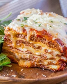 a wooden plate topped with lasagna covered in sauce and cheese next to a salad