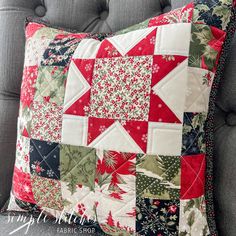 a red and green patchwork pillow sitting on top of a gray couch