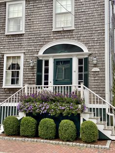 a house with green shutters and purple flowers on the front steps in front of it